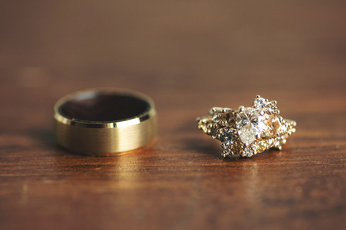 A gold wedding band and a gold diamond engagement ring displayed on a wooden surface.