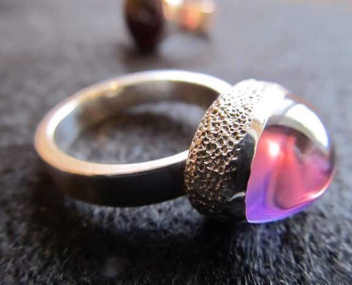 Silver ring with textured band and pink gemstone on a dark surface