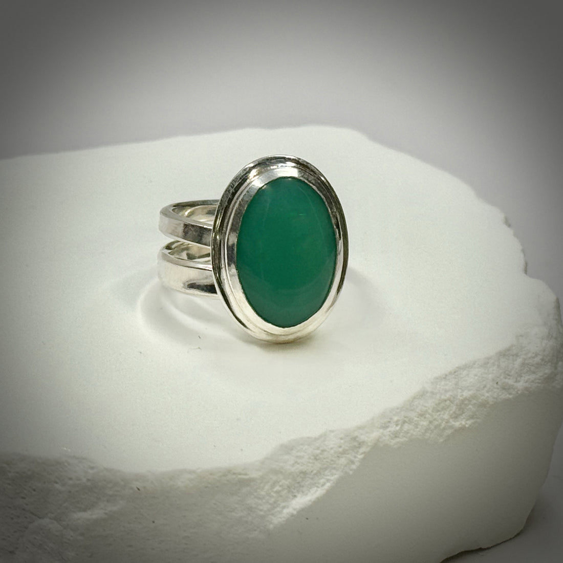 Silver ring with a green stone on a white stone surface