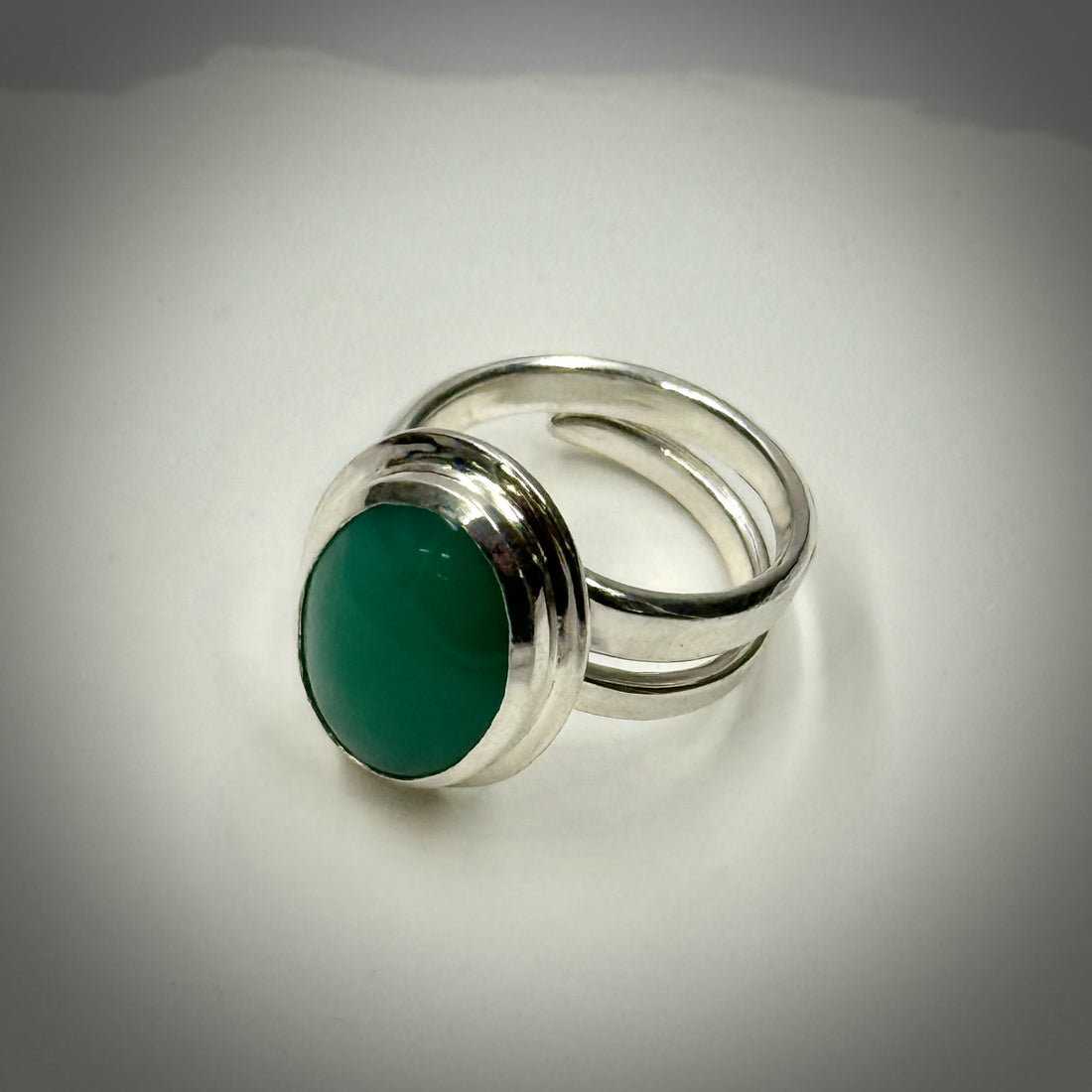Silver ring with a green gemstone on a light gray background